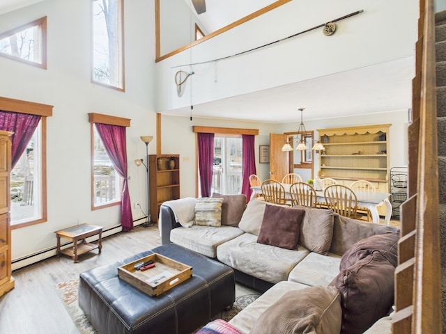 living room featuring light wood-style floors, a baseboard radiator, a high ceiling, and an inviting chandelier