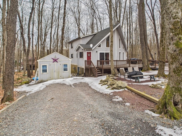 view of front of house with a storage shed, roof with shingles, a deck, and an outdoor structure