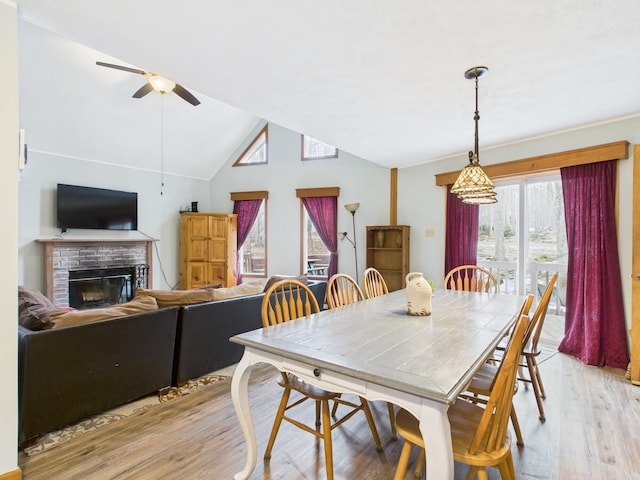 dining space with vaulted ceiling, a brick fireplace, a ceiling fan, and light wood-style floors