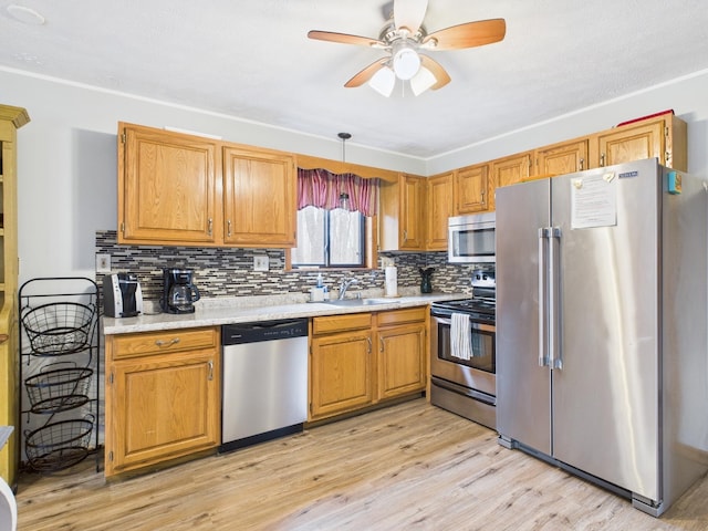 kitchen with a sink, light countertops, appliances with stainless steel finishes, light wood-type flooring, and tasteful backsplash