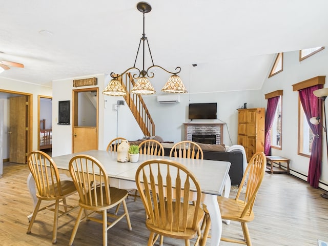 dining area featuring lofted ceiling, light wood-style flooring, ceiling fan, a wall mounted air conditioner, and a brick fireplace