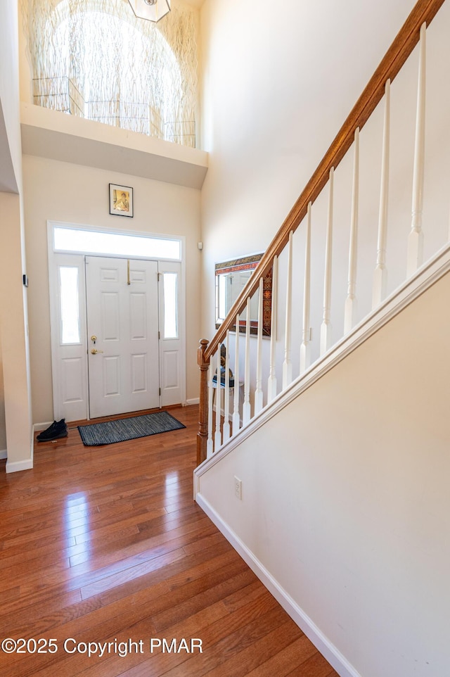 entrance foyer with plenty of natural light, baseboards, a towering ceiling, and wood-type flooring