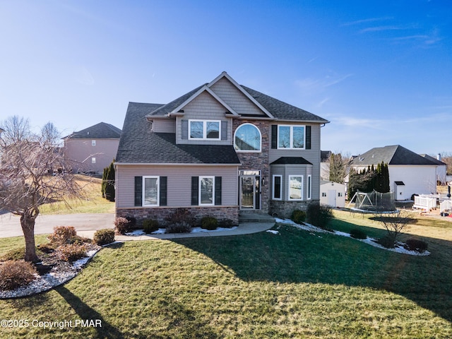 view of front of home featuring stone siding, a trampoline, roof with shingles, and a front lawn