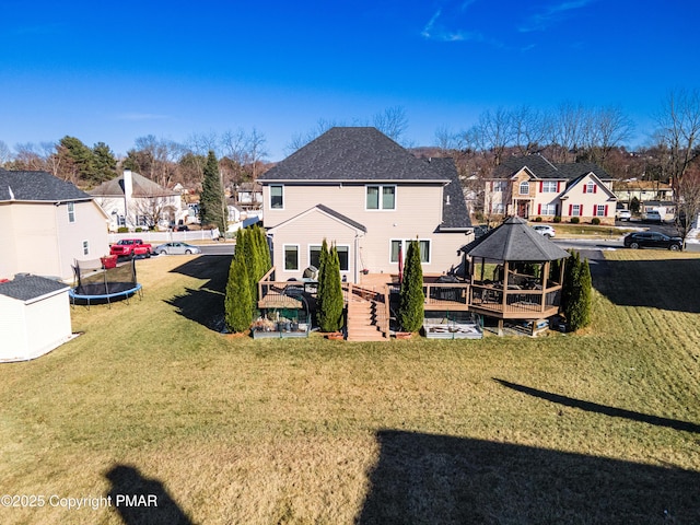 back of property featuring a yard, a trampoline, and a wooden deck