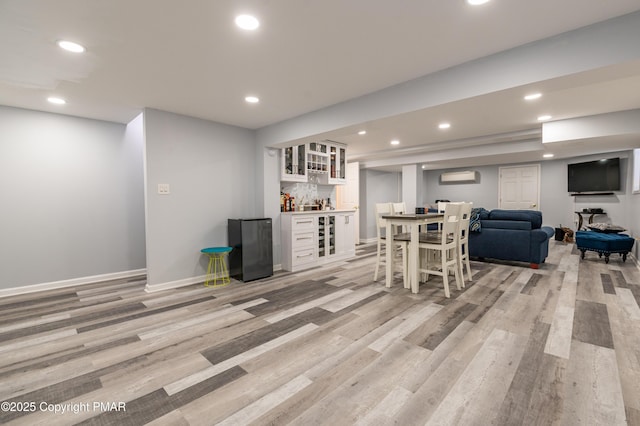 bar with a wall unit AC, white cabinets, black refrigerator, and light hardwood / wood-style flooring