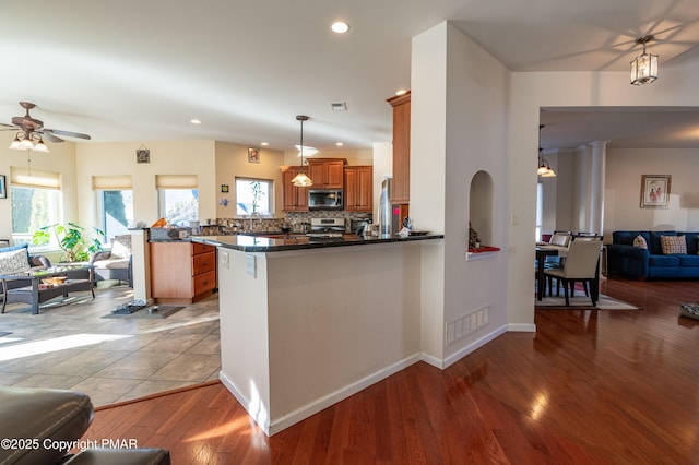 kitchen with appliances with stainless steel finishes, light hardwood / wood-style floors, pendant lighting, backsplash, and kitchen peninsula