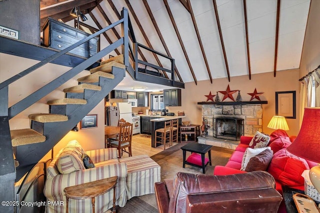 living room with light wood finished floors, beamed ceiling, stairs, a fireplace, and high vaulted ceiling