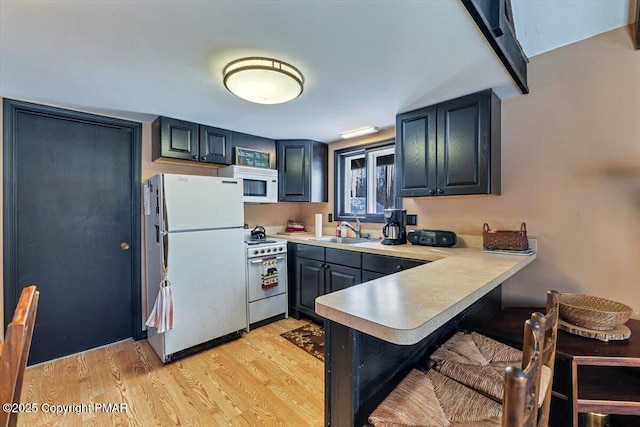 kitchen with a peninsula, white appliances, a sink, a kitchen breakfast bar, and light wood-type flooring