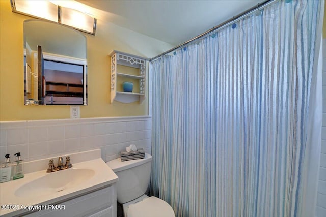 full bathroom with curtained shower, toilet, vanity, tile walls, and wainscoting