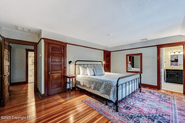 bedroom with visible vents, ensuite bath, baseboards, and wood finished floors