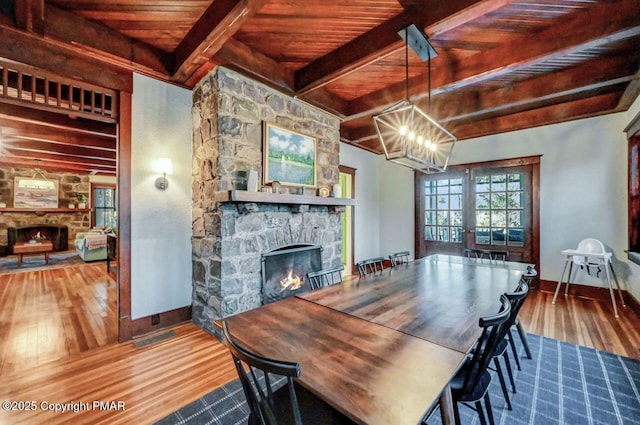 dining space with wood-type flooring, baseboards, a stone fireplace, and beam ceiling