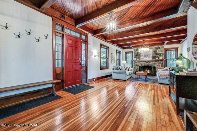 foyer entrance featuring wood ceiling, wood-type flooring, beamed ceiling, an inviting chandelier, and a stone fireplace