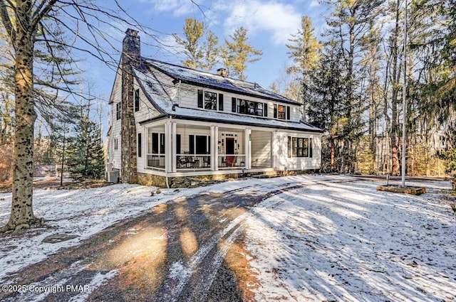 view of front of house with driveway, covered porch, a chimney, and cooling unit