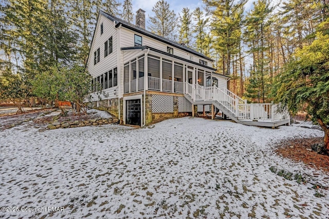 snow covered rear of property with stairs, a chimney, and a sunroom