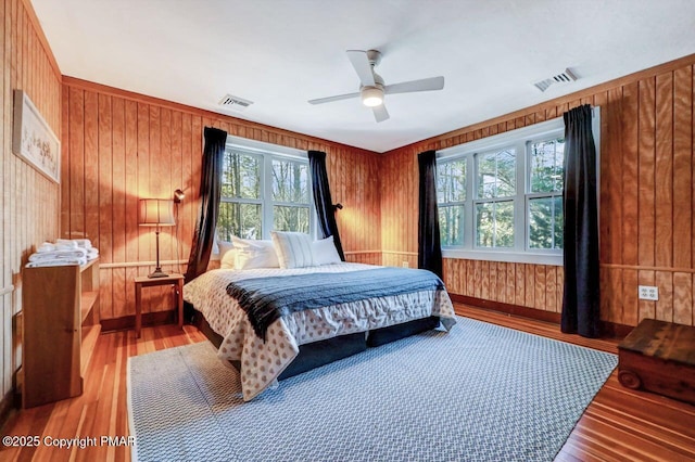 bedroom featuring ceiling fan, wood walls, light wood-type flooring, and visible vents