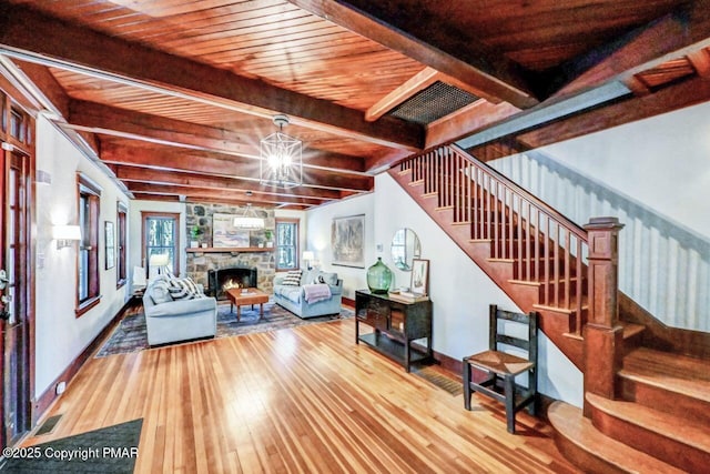 living area featuring hardwood / wood-style flooring, a notable chandelier, stairs, a stone fireplace, and beam ceiling