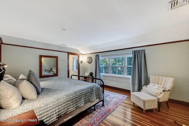 bedroom featuring lofted ceiling, visible vents, baseboards, and wood finished floors