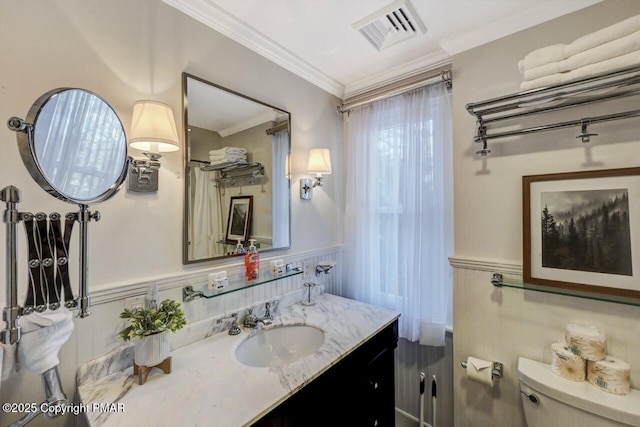 bathroom featuring toilet, a wainscoted wall, vanity, visible vents, and ornamental molding