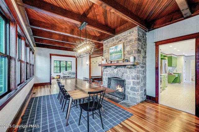 dining area with a stone fireplace, wood finished floors, wood ceiling, beam ceiling, and an inviting chandelier