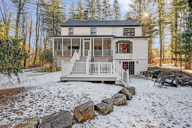 snow covered rear of property with a sunroom and stairs