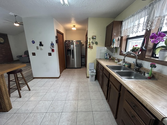 kitchen featuring stainless steel refrigerator with ice dispenser, a sink, light countertops, light tile patterned floors, and ceiling fan