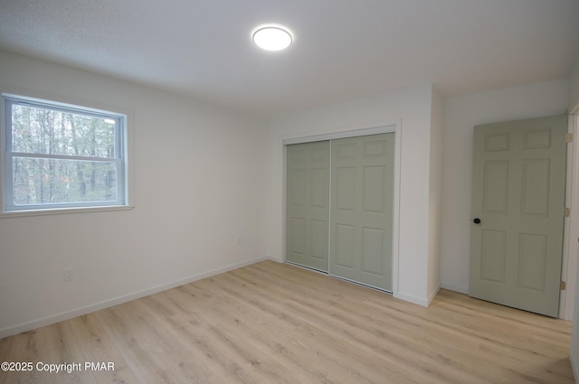 unfurnished bedroom featuring a closet, light wood-type flooring, and baseboards