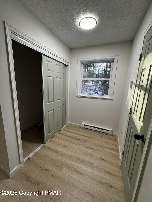 interior space featuring a baseboard heating unit, a closet, baseboards, and light wood-style floors