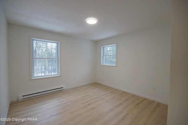 empty room with baseboard heating, light wood-style flooring, and baseboards