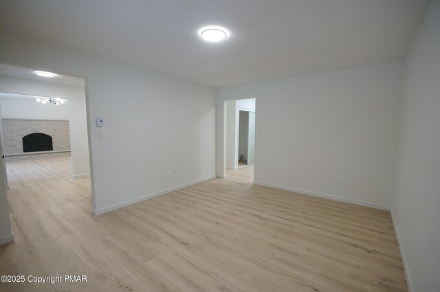 spare room with light wood-type flooring, a fireplace, and baseboards