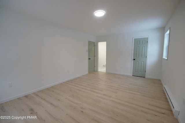 empty room featuring a baseboard radiator, baseboards, and light wood finished floors