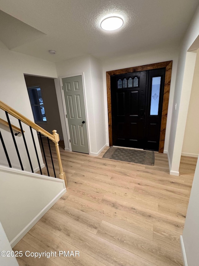 foyer with baseboards, stairway, light wood finished floors, and a textured ceiling