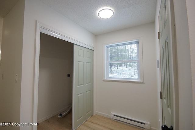 doorway featuring a baseboard heating unit, light wood-style flooring, a textured ceiling, and baseboards