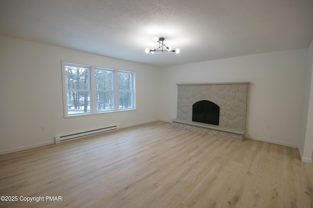 unfurnished living room featuring a textured ceiling, a stone fireplace, a baseboard heating unit, baseboards, and light wood-type flooring