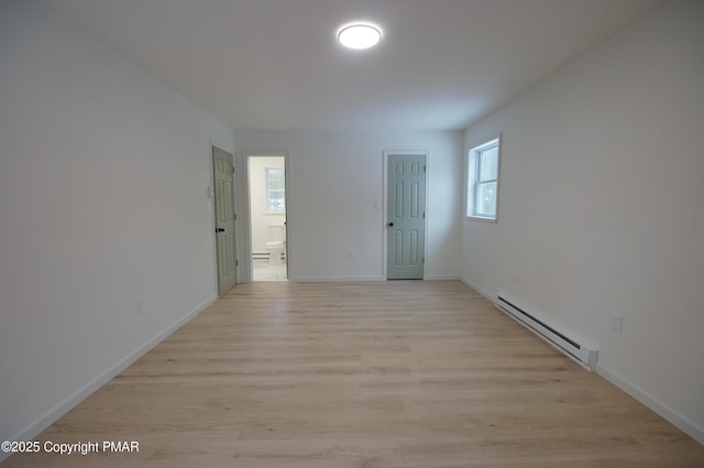 empty room featuring a baseboard radiator, baseboards, and light wood finished floors