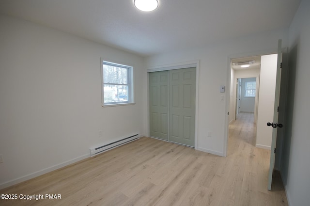 unfurnished bedroom featuring multiple windows, a baseboard radiator, a closet, and light wood-style flooring