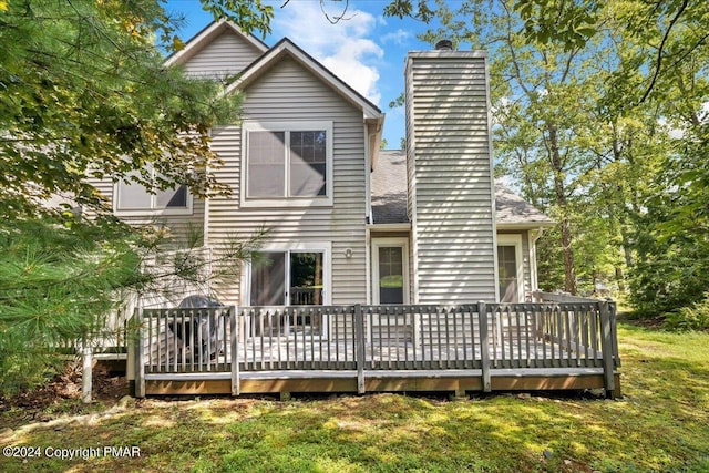 back of house featuring a chimney, a lawn, and a wooden deck