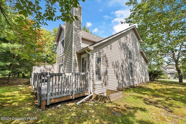 view of property exterior with a lawn, a chimney, and a wooden deck