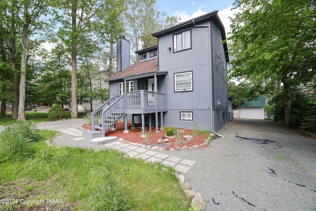 rear view of property featuring driveway, stairs, and a chimney