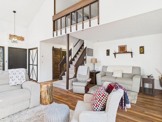 living area with a notable chandelier, stairway, a barn door, wood finished floors, and high vaulted ceiling