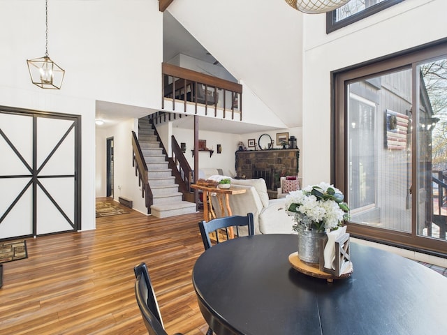 dining room featuring a notable chandelier, stairway, a towering ceiling, a stone fireplace, and wood finished floors