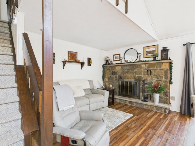 living room with a stone fireplace, stairway, and wood finished floors