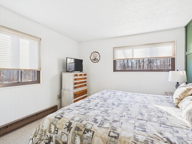 carpeted bedroom with a baseboard heating unit and a textured ceiling