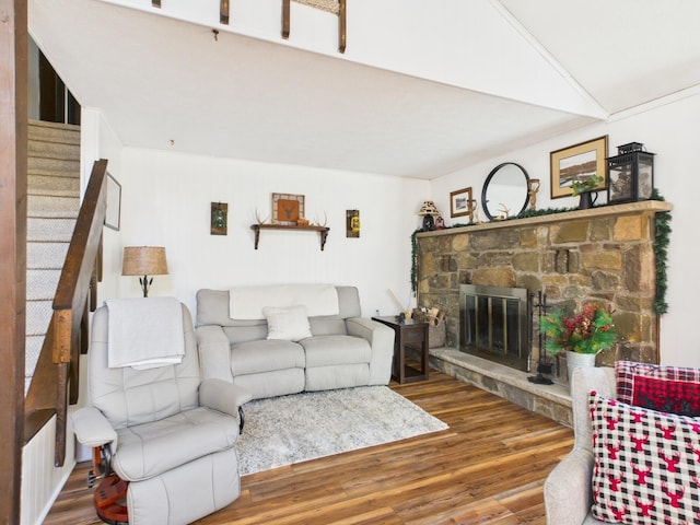 living area featuring a stone fireplace, stairway, and wood finished floors