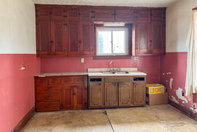 kitchen with a textured ceiling, light countertops, wainscoting, and a sink