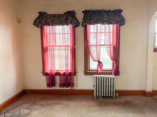 carpeted spare room featuring radiator, baseboards, and arched walkways