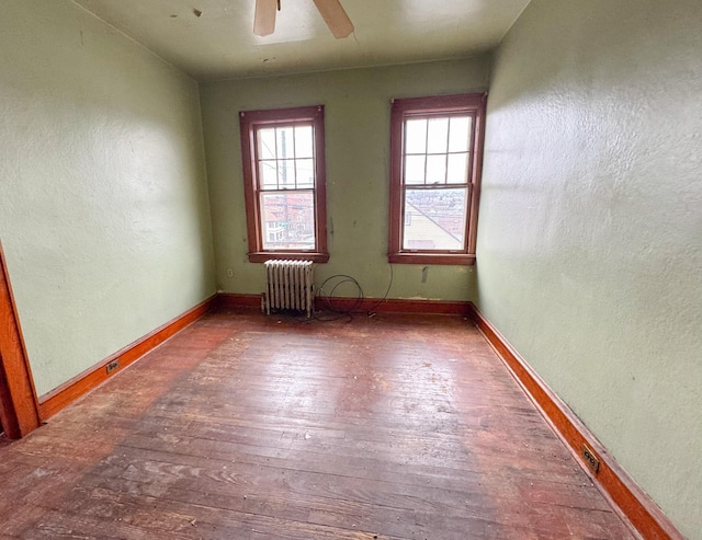 spare room featuring a textured wall, a ceiling fan, baseboards, radiator, and hardwood / wood-style floors