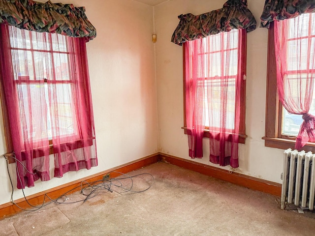 carpeted empty room with radiator heating unit and baseboards