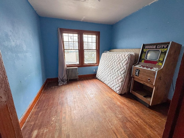 bedroom with radiator heating unit, wood-type flooring, and baseboards