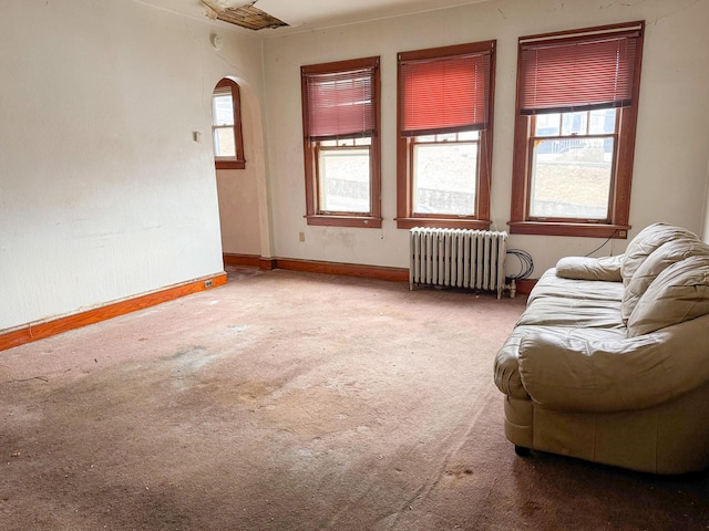 sitting room featuring radiator, carpet, baseboards, and arched walkways