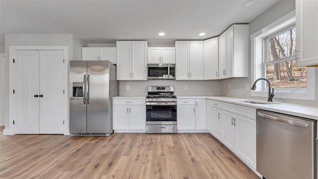 kitchen with appliances with stainless steel finishes, a sink, light wood-style floors, and white cabinets